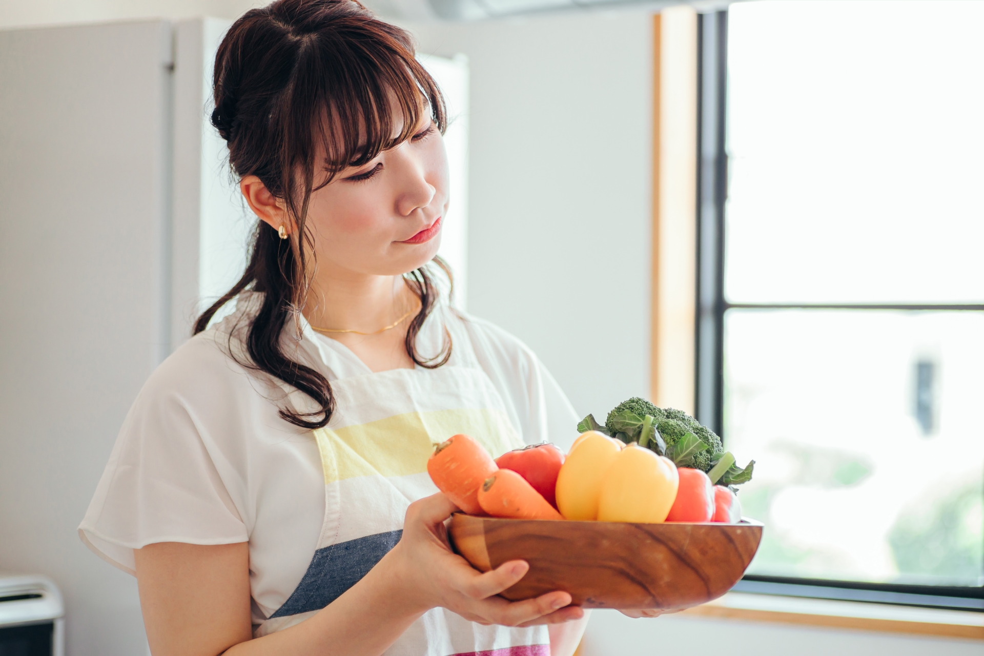 野菜が入った大皿を持ちながら悩む女性の写真