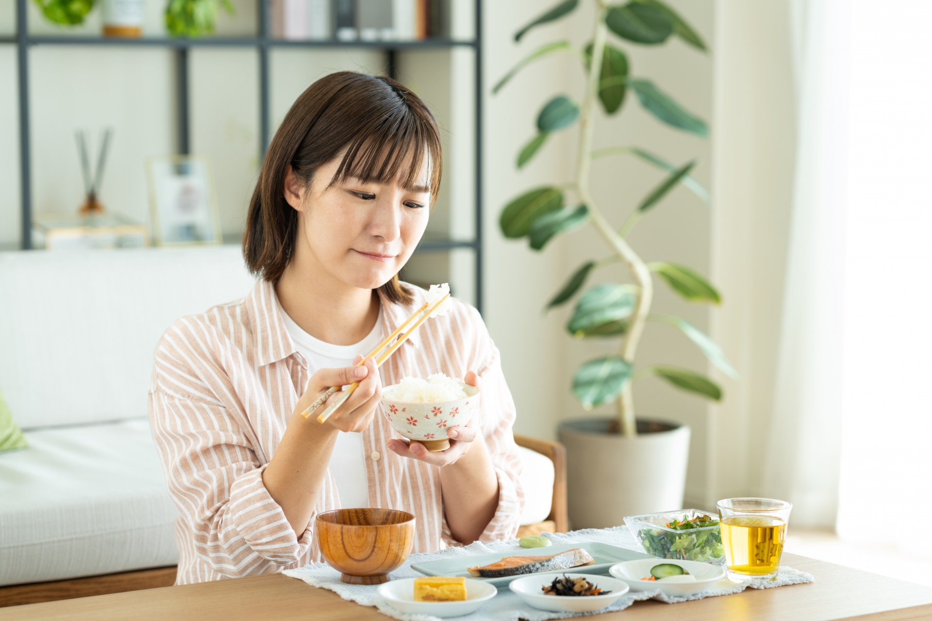 ご飯をお箸で持って悩む女性の写真